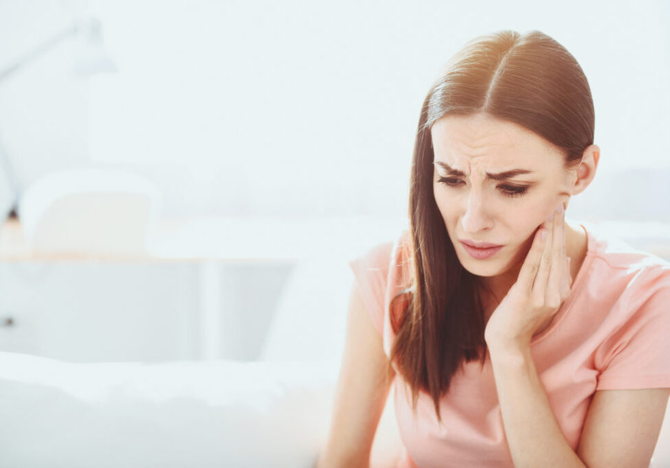 Unstoppable pain. Beautiful brunette woman grimacing and touching her jowl while having toothache.